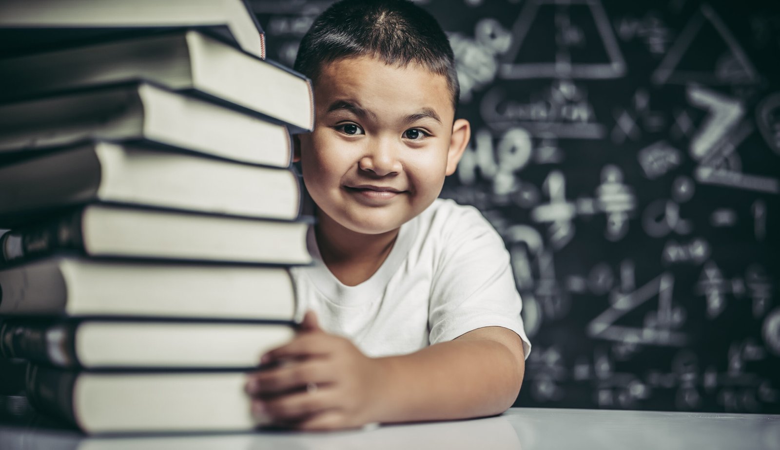 A boy hugging a pile of books in the classroom.